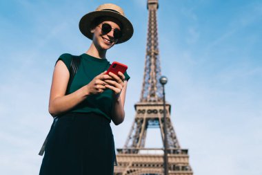 Ağ üzerinden telefon görüşmesi yaparken cep telefonuyla konuşan mutlu kadın blogcu. Hasır şapkalı gülümseyen kadın. Eiffel Kulesi ile Paris 'teki romantik Fransız tatillerinden alıntılarla mesaj yazıyor.