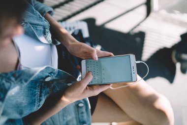 Beyaz gömlekli, kot ceketli, akıllı telefonlu, sokakta dinlenirken bankta oturan yüzsüz bir kadından.