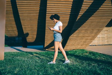 Kotlu, çekici, koyu tenli hippi kız. Güneşli bir günde akıllı telefondan sohbet ediyor. Mutlu Afro-Amerikan milenyum hipster kızı cep telefonundan e-postalarını kontrol ediyor.