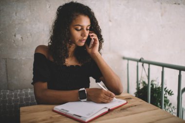 Akıllı telefon planlama toplantısıyla ilgili konuşurken 20 'li yaşlardaki konsantre Afro-Amerikalı kadın cep telefonuyla arayıp not alıyor.