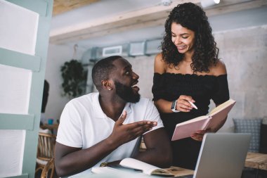 Başarılı esmer tenli erkek ve kadın meslektaşlar işbirliği yapmayı tartışıyor notları birlikte kontrol ediyorlar, gülümseyen Afrikalı Amerikalı öğrenciler danışmanlık eğitimi alıyorlar ve teknolojiyi kullanıyorlar.