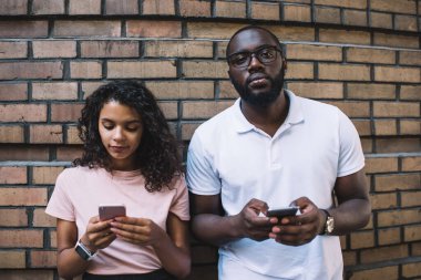 Ciddi koyu tenli, bin yıllık sakallı bir adam cep telefonuyla kameraya bakıyor. Cihazlara bağımlı postalar gönderiyor. Afro-Amerikan kadın ve erkek arkadaşları duvarın yanında durmuş gerçek iletişimi görmezden geliyorlar.