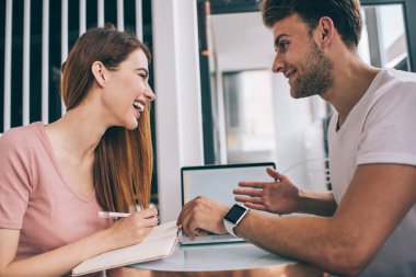 Erkekle buluşurken ve kafede dizüstü bilgisayarla tartışırken kitaptan gülen neşeli genç bayanın yan görüntüsü 