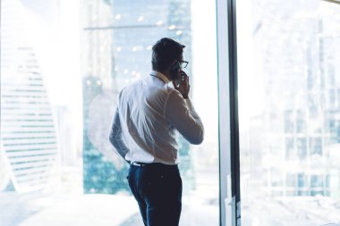Resmi kıyafet ve gözlüklü adamın, iş arkadaşını aramak için cep telefonu kullanması modern ofis binasının penceresinden bakan şirketin stratejisini tartışması.