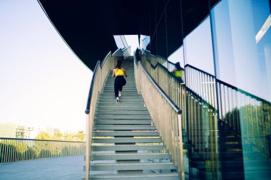 Moda eşofmanlı aktif bir bayan atletin şehir merdivenlerinde yürüyüş yaparken dışarıda fiziksel dinlenmenin tadını çıkarırken, şehirde mükemmel vücut şekli eğitimi almış güzel bir koşucu.