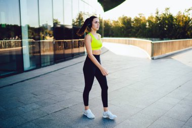 Spor elbiseli genç bir kadın ve kulaklıklı beyaz spor ayakkabılar güneşli bir günde sokakta spor yapan kulaklıklı bir kadın.
