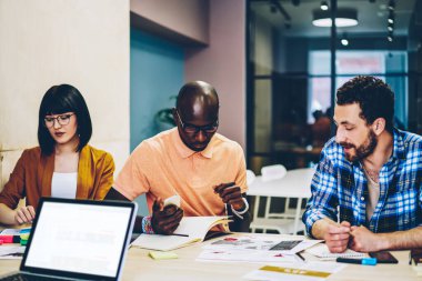 Çok ırklı iş ortakları strateji geliştirir ve fikirleri paylaşırken boş ekranlı dizüstü bilgisayarla masaya oturur ve çağdaş açık uzay ofisinde raporlar sunarlar.
