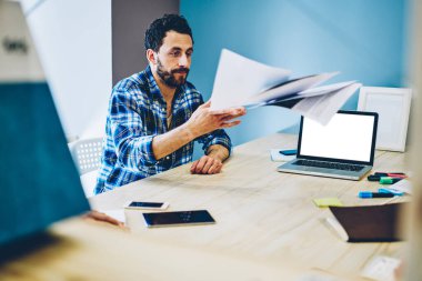 Modern konferans odasında dizüstü bilgisayarında boş bir ekranla otururken iş ortaklarıyla görüşmelerin başarısızlıkla sonuçlanmasının ardından gündelik kıyafetlerle gezen ve belgeleri masaya atan dalgın girişimci.