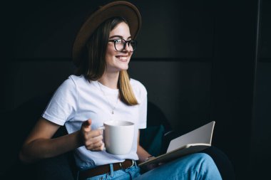Görme düzeltmesi için göz giysisi giyen neşeli beyaz kız hobi ve çaya zaman harcıyor, 20 'li yaşlarda elinde ilginç bir kitap ve aroma kahvesi tutan 20' li yaşlarda bir kadın kafede boş vakit geçirmekten memnun.