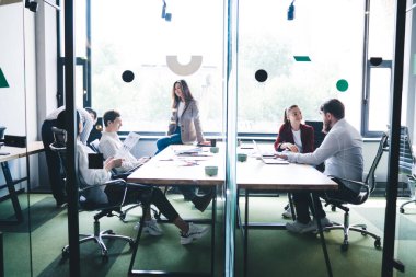 Ofis odasında cam duvarla konuşan ve birlikte çalışan bir grup odaklanmış iş arkadaşı.