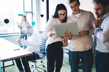 Bir grup konsantre ve düşünceli ofis çalışanı koridorda durup gülerken bilgisayarın ekranına bakıyorlar.