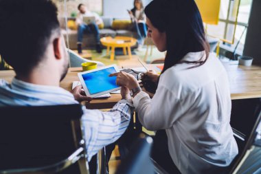 Arka plan tanınmayan ofis çalışanları mavi ekranlı tablet üzerinde çalışırken arka planda bulanık çalışma alanı olan bir masada oturuyorlar.