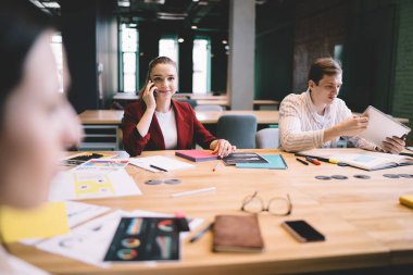 Resmi olarak neşeli yetişkin bayan çalışanlar toplantı masasında oturmuş şirkette çalışma planını tartışırken cep telefonuyla konuşan belgelerle birlikte giyiniyorlar.