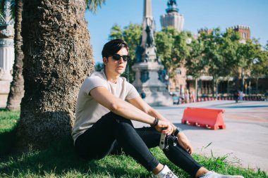 Parkta oturup hobisine zaman harcayan neşeli, yakışıklı hippi portresi. Elinde güneş gözlüklü gezgin adam. Tatilde şehri ziyaret ederken fotoğraf çektiği için elinde kamera var.