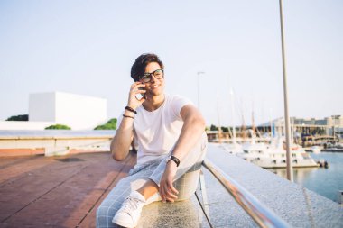 Gülümseyen hippi genç gezginin portresi. Hafta sonları güneşli bahar günlerinde yat ve gemilerle birlikte koyda oturuyor. Mutlu 20 'li yaşlarda şık giyinmiş bir adam gezintide cep telefonuyla konuşuyor.