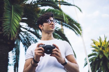 Gözlüklü yetenekli erkek fotoğrafçı. Kamera tutuyor. Açık havada çalışıyor. Şehirde resim çekiyor. Kafkasyalı turist açık havada eğleniyor ve aktif tatillerin fotoğrafını çekiyor.