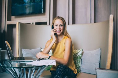 Tatmin olmuş kadın yönetici cep telefonuyla konuşuyor ve kafede rahat bir kanepede oturmuş kameraya bakarken projeyi tartışıyor.