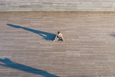 Tanınamayan barışçıl bir kadının yoga yapması ve uzun bir gölgenin yanında, ahşap zeminde meditasyon yapması. 