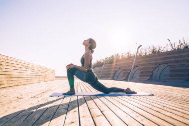 Spor kıyafetli, esnek, esnek bir kadının sabah güneşli terasta tek başına Asya 'ya diz çöküp antrenman yapması.