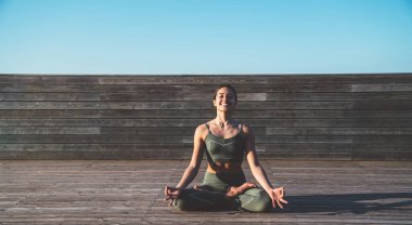 Nilüfer pozisyonunda neşeli, sakin, dişi yogi dizlerinin üzerinde elleri ve gün doğumunda ahşap kaldırımda gözleri kapalı