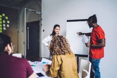 Boş tahtaya odaklanan ve modern ofiste projeyi tartışırken Afrikalı Amerikalı uzmanların fikirlerini dikkatle dinleyen iş ortakları memnuniyet verici.