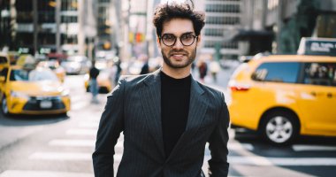 Finansal bölgede kameraya gülümseyen, iş adamı pozu veren, lüks takım elbise ve optik gözlük giyen mutlu başarılı girişimcinin yarım boy portresi.