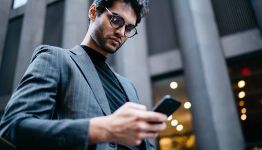 Görüş düzeltimi için optik gözlüklerle gurur duyan erkek CEO 'nun altında. Finansal web sitesinde pazar haberlerini kontrol etmek için yüksek hızlı internet bağlantısı ve bankacılık uygulaması olan akıllı telefon aygıtı kullanılıyor.