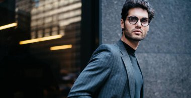 Yakışıklı Avrupalı girişimcinin yarı boy portresi lüks takım elbise ve görüş düzeltmesi için optik gözlük takmış finans bölgesindeki kameraya bakıyor, iş adamı şehir merkezinde poz veriyor.