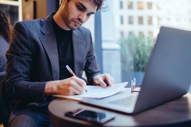 Eğitimli erkek girişimci moda kıyafetleri içinde başarılı planlar yapıyor kafeterya masasında dizüstü bilgisayarla oturuyor, resmi giyinmiş yetişkin öğrenci düzenleme bilgileri kurs ödevi