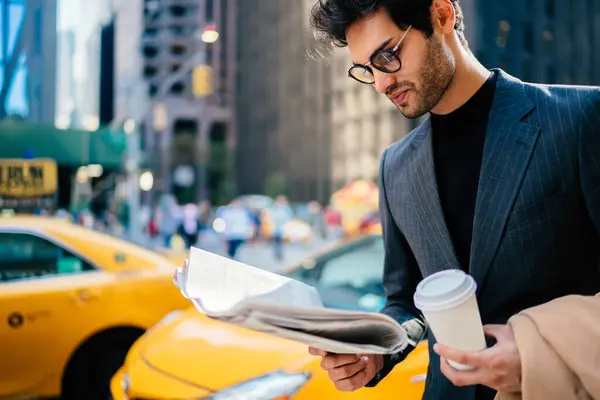 Trendy dressed investor in stylish clothing reading business news about corporate merger of financial firms, European male lawyer in formal clothing checking article on journal during morning coffee