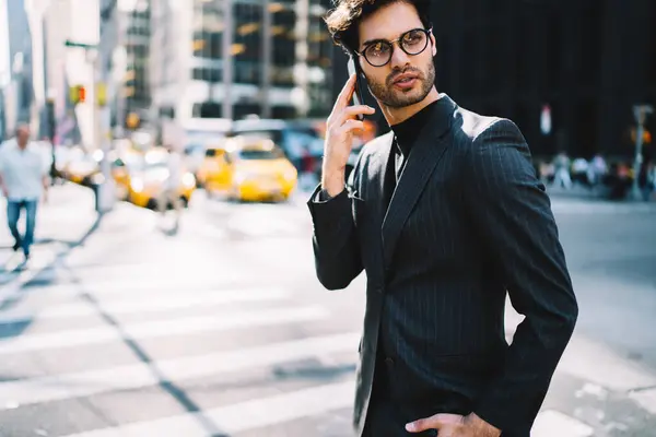 Successful man in stylish suit using roaming internet connection for making international smartphone call via cellphone application on mobile technology, formally dressed businessman phoning