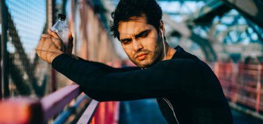 Elektronik ekipmanlı erkek sporcu motivasyon sesli kitabı için şehir merkezinde sabah antrenmanı için dışarıda düşünceli düşünce, modern kulaklıklar takan dalgın sporcu.