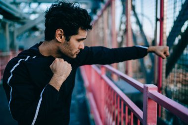 Eşofmanlı güçlü vücut geliştiricinin kenar mahalle ortamında fiziksel egzersizler yapmaya hazırlanması, Avrupalı sporcunun sabah sporu sırasında enerji ile boks yumrukları denemesi.