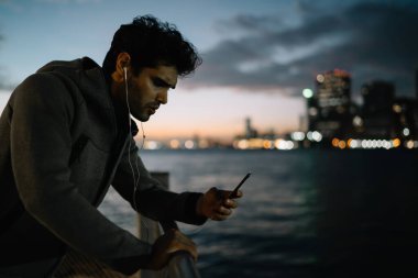 Erkek sporcu, akıllı telefon zımbırtısıyla içerik spor blogunda makale okurken spor hakkında sesli kitap dinlerken arkadaşına mesaj yazan genç adam akşam koşusu hakkında sorular soruyor.