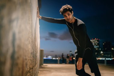 Şehir ortamında her akşam duvara yaslanan yorgun genç bir adamın portresi, modern şehirde antremandan sonra kulaklıkla müzik dinleyen eşofmanlı yorgun bir erkek sporcu.