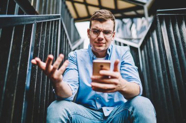 Şaşırmış milenyum blogcusu, yayınlama indirme hatasıyla karışık akıllı telefon internet bağlantısıyla sorun çözme, cep telefonuyla arama yaparken gözlüklü hippi adam kötü haber okuyor.