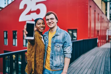 Modern cep telefonu cihazını tanıtmak için reklam çekimi sırasında kameraya gülümseyen çok kültürlü erkek ve kadın arkadaşlarının yarım boy portresi.