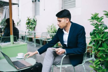 Kafe terasında dizüstü bilgisayarla oturan ciddi Hintli erkek girişimci. Uzaktan kumandalı işten memnun, resmi kıyafetli yakışıklı, düşünceli adam blogcu. Proje üzerinde uzaktan kazanç sağlıyor.