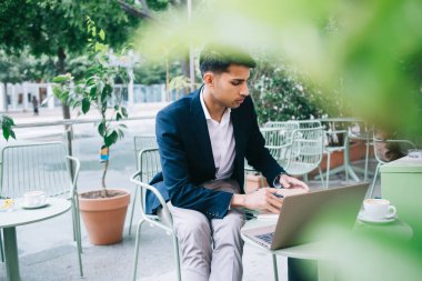 Ciddi yetenekli, modaya uygun resmi yönetici. Laptop bilgisayarla kafe terasında çalışıyor. Yakışıklı Hindu müreffeh iş adamı online projeden ve açık hava işinden memnun.