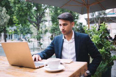 Ciddi ciddi gururlu erkek CEO çevrimiçi haberleri okuyor ve dışarıda dizüstü bilgisayarda postaları kontrol ediyor, modaya uyan zengin Hindu işadamı terasta uzaktan kumandalı bir işte video izliyor.