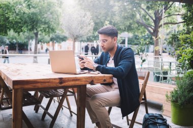 Kendine güvenen erkek CEO laptopta uzaktan çalışıyor. Sosyal ağlarda haberleri akıllı telefondan kontrol ediyor. Yakışıklı Hindu iş adamı dışarıda dizüstü bilgisayarla serbest çalışıyor.