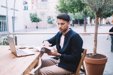 Serbest çalışmaktan ve terasta kişisel eğitim edebiyatı okumaktan hoşlanan yakışıklı Hintli hippi, modaya uygun giyim ve gözlüklü ciddi işadamı dizüstü bilgisayar ve kitapla uzaktan çalışma üzerine oturuyor.