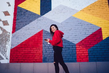 Tasasız hippi kızın yarım boy portresi modaya uygun giyinmiş kameraya bakıyor ve kentselliğe gülümsüyor duvarında şık bir sokak sanatıyla yürüyor, akıllı telefonlu mutlu bir milenyum.