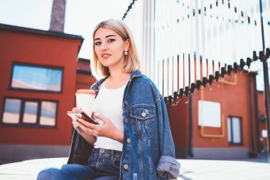 Kentte poz vermek için elinde cep telefonu teknolojisi ve kahve olan modaya uygun kadın blogcu portresi. Şehir merkezinde gezici aletlerle gezen çekici hippi kız.