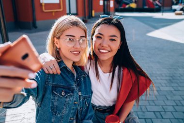 Mutlu arkadaşlarının portresi akıllı telefon kamerasına gülümsüyor. Selfie çektikleri için içeriği etkiliyor. Şehir merkezinde dinlenen neşeli hippi kızlar fotoğraf çekmek için cep telefonu teknolojisini kullanıyorlar.