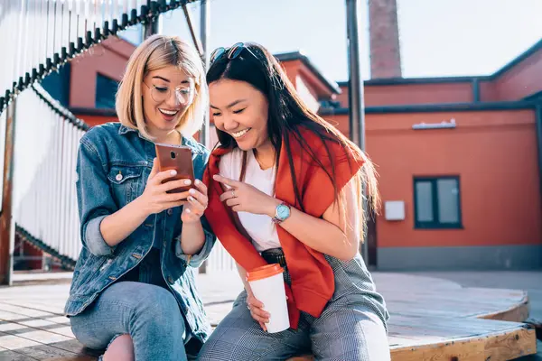 两个快乐的千禧年嬉皮士女孩通过现代手机搜索信息 快乐的女性朋友们通过智能手机聊天程序阅读着积极的短信 — 图库照片