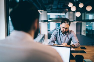 Ofisteki iş toplantısında bilgisayarını boş ekranla kullanan, gözlüklü, düşünceli bir yönetici.