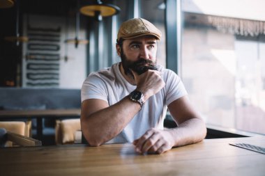 Kafeterya 'nın kafeterya ziyaretçisi, kafenin yanında oturmuş, fikirlere ve gelecek planlarına kafa yoruyor. Şapkalı, sakallı, ciddi bir adam ve son moda kol saati.