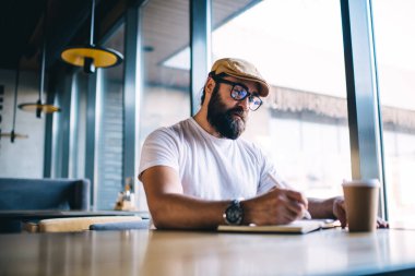 Kafkas sakallı, vizyon düzeltme için göz giysisi yazan, kafenin içinde serbest çalışan, düşünceli, olgun bir adam boş zamanlarında fikir ve planları not alıyor.