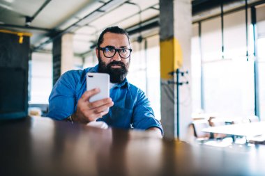 Kafeteryadaki barda oturup sohbet etmek için cep telefonu tutan, ciddi bir beyaz erkek. 40 'lı yaşlarda, kendine güvenen, küçük işletme sahibi, akıllı telefondan 4G bağlantısı ile posta gönderen biri.